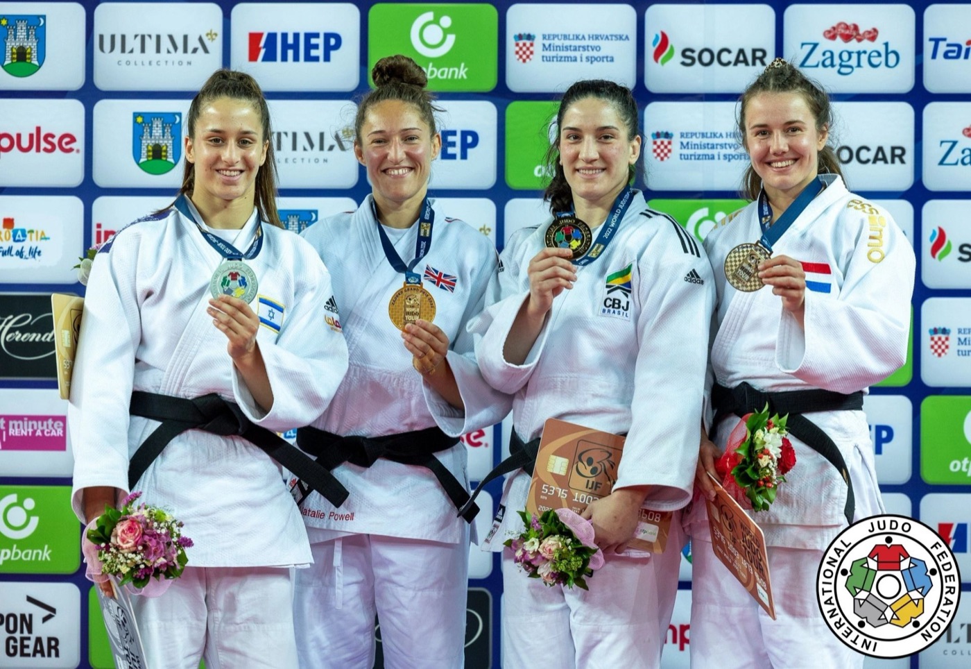 Four judoka hold up their medals on the podium at the Zagreb Grand Prix, Inbar Lanir on the left in a white judogi.